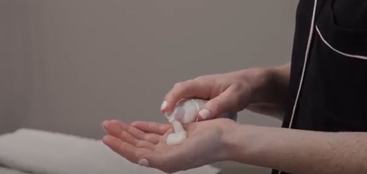 White foaming facial cleanser pumped out bottle onto woman's hand.