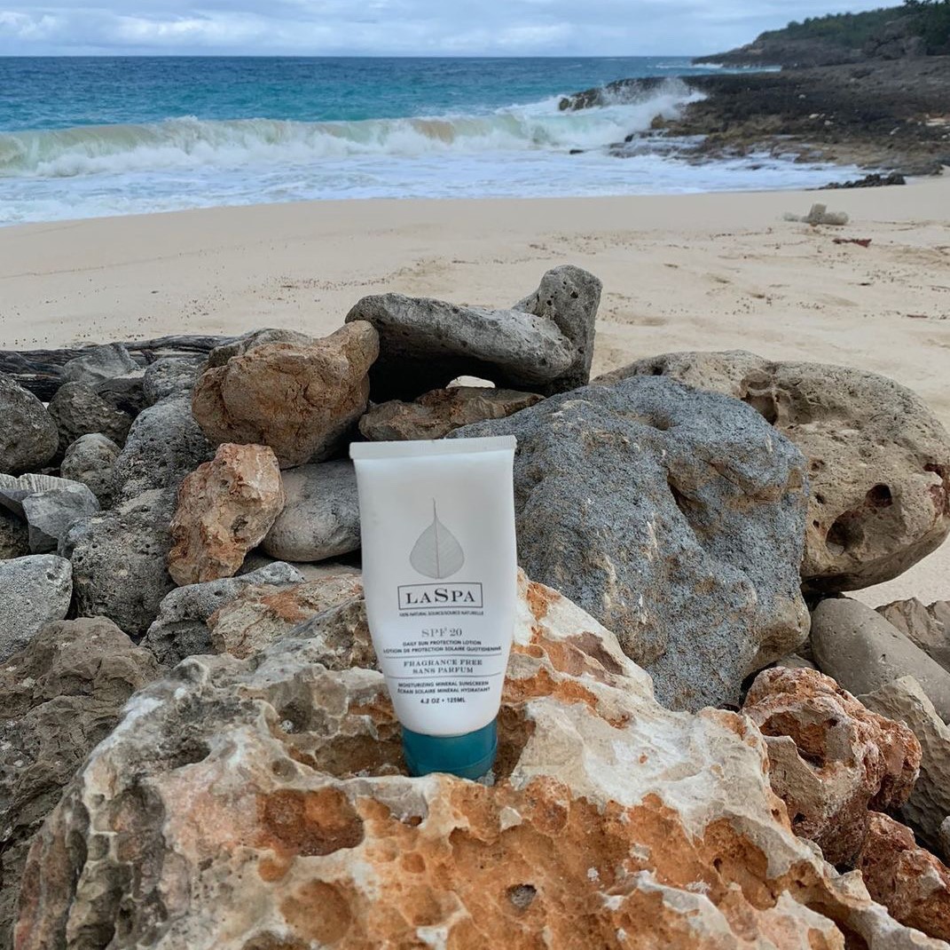 LASPA SPF 20 mineral based sunscreen standing upright on a bed of rocks on the beach
