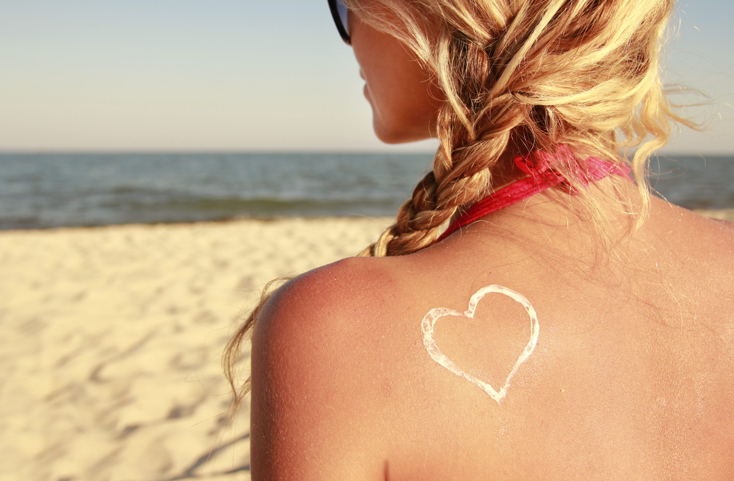Caucasian woman looking out at the beach and has a zinc oxide SPF sunscreen applied on her back in the shape of a heart.